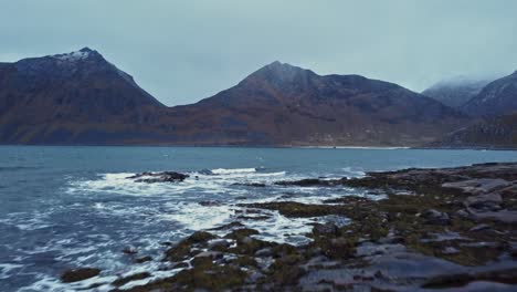 waving sea surrounded by rocky mountains under overcast sky