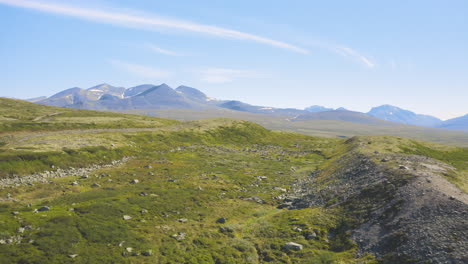 rocky green fields with mountains and blue sky in the background in rondane national park, norway