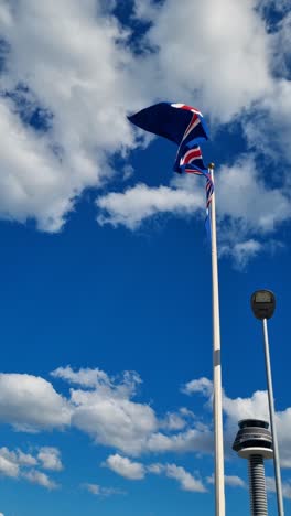 the icelandic flag sways gently in the wind beneath a blue sky scattered with white clouds, with the arlanda airport control tower visible in the background