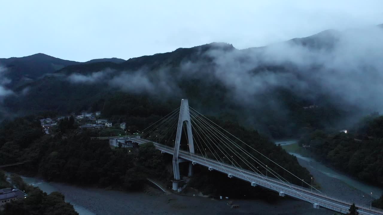 alto dron aéreo sobre el espeluznante valle de niebla rural al atardecer con puente y barranco - vuelo hacia adelante