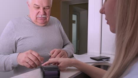 senior man paying with credit card via payment terminal at clinic