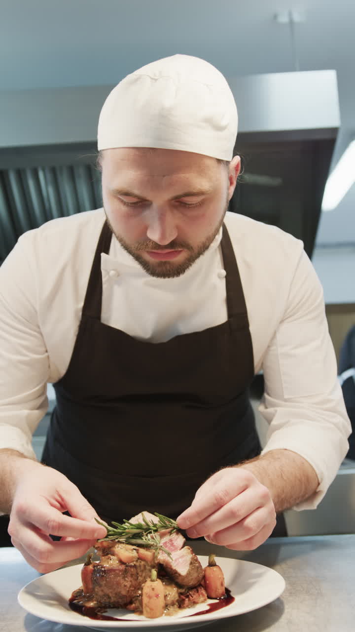 Focused caucasian male chef decorating prepared meal on plate in kitchen, slow motion, vertical