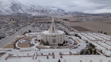 aerial orbit shot of beautiful architecture named, payson utah temple, lds mormon church with dramatic snow covered mountain landscape and grey clouds