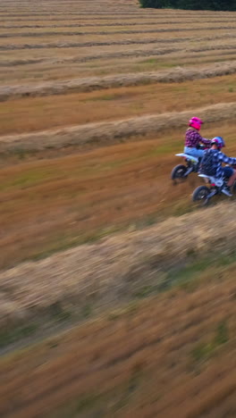 young couple riding motorcycles close to each other. people having fun in the field with mowed grass at setting sun. view from above. vertical video