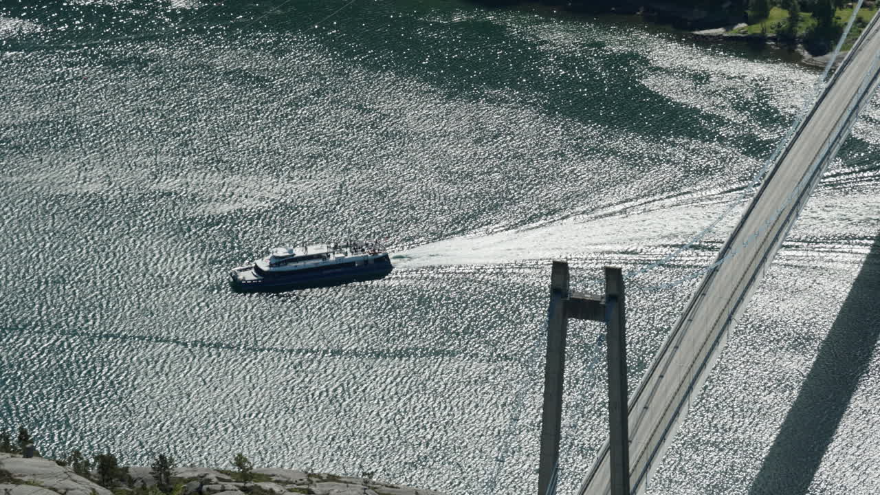 Ship traveling on the Lysefjord in Norway. The Lysefjord Bridge is visible above the ship. The sun is reflected in great detail on the waves of the fjord