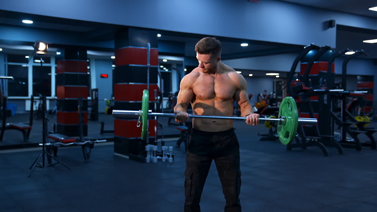 Athletic man in gym exercising with barbell. Bodybuilder with perfect body. Naked torso with perfect abs.