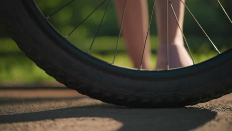 close-up of individual legs in pink sneakers as they kick a bicycle tire to check air pressure, lush greenery and trees create a vibrant background, casting playful shadows on the ground