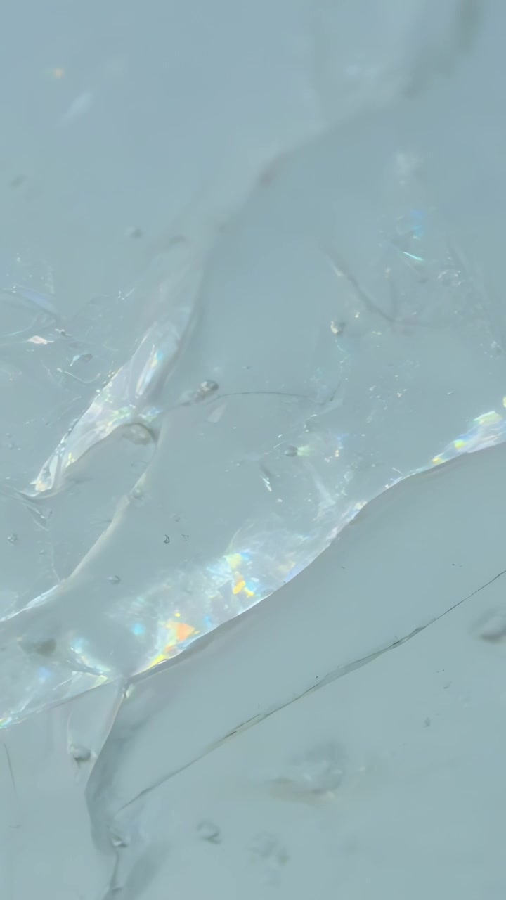 垂直影片：輕微移動後晃動的薄膜，在淺色微距底座上投射出棱鏡般的光芒，並顯示出灰塵。
