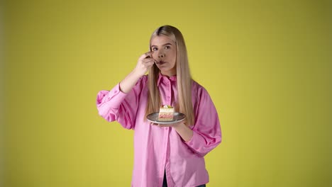 young blonde woman holding plate of cake and eating with fork, studio portrait