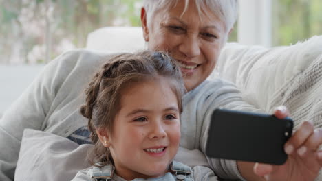 Kleines-Mädchen-Nutzt-Smartphone-Mit-Großmutter-Beim-Videochat,-Winkt-Der-Familie-Zu-Und-Teilt-Ihr-Urlaubswochenende-Mit-Oma,-Die-Auf-Dem-Handy-Chattet-Und-Sich-Zu-Hause-Mit-Enkelin-In-4k-Entspannt