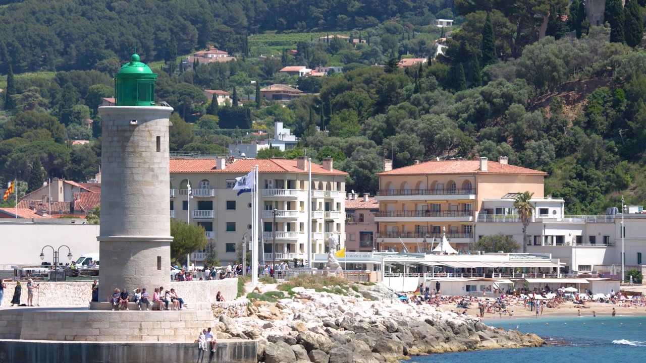 Inquadratura ampia statica di un faro in pietra che domina una città portuale mediterranea e montagne rigogliose