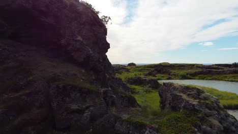 Ascending-aerial-shot-above-rocky-hill-with-beautiful-Icelandic-river-landscape-and-Ocean-in-background