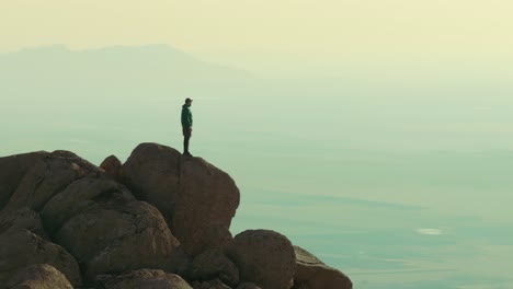 Lone-hiker-stands-atop-a-towering-mountain-peak