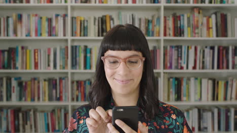 retrato de una joven estudiante usando un teléfono inteligente estantería de la biblioteca de la universidad