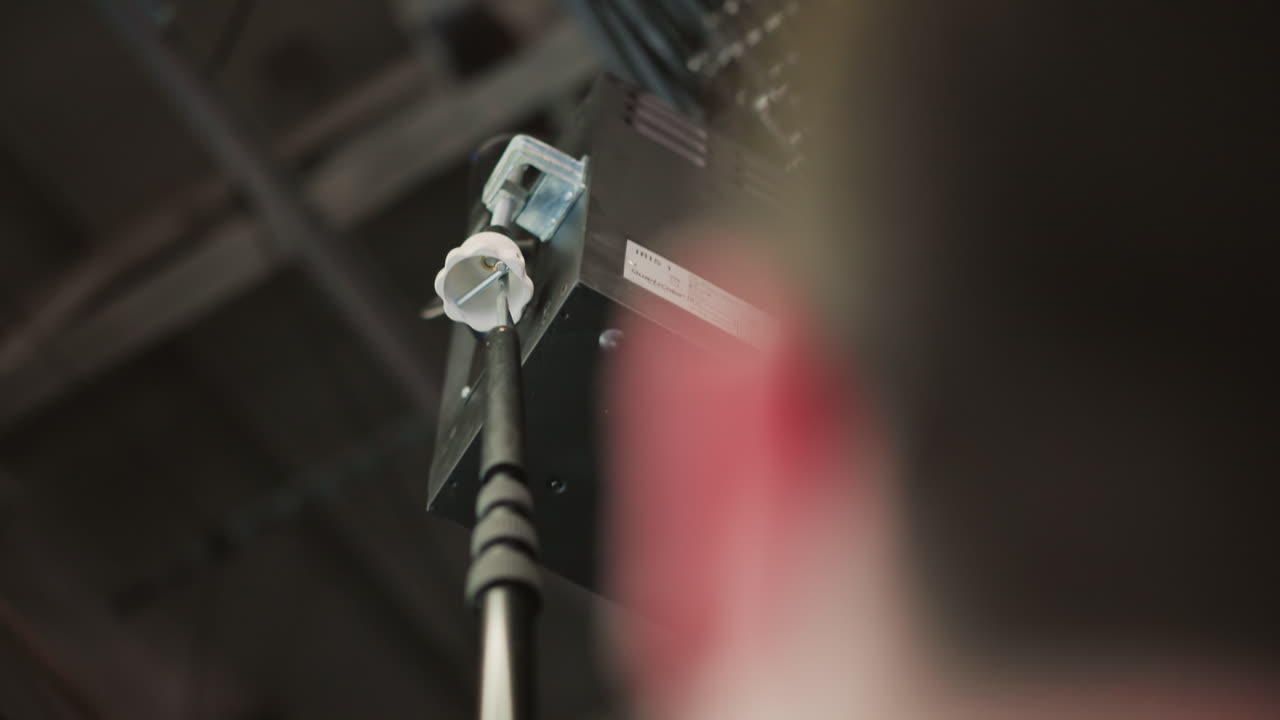 Close-up of boom pole in broadcast studio, technician adjusting it to control lighting equipment. Professional media production environment with visible camera setup and lighting fixtures