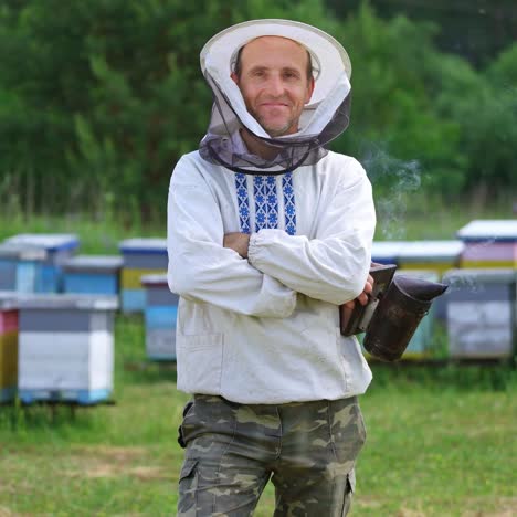 portrait of beekeeper man. apiarist in white shirt and protective hat holding chimney with smoke and smiling on camera. beekeeper at the apiary.
