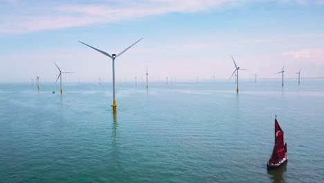 A-flat-bottomed-sailing-barge-sailboat-moves-up-the-Thames-Río-Estuary-in-England-amidst-numerous-wind-turbine-windmills-2