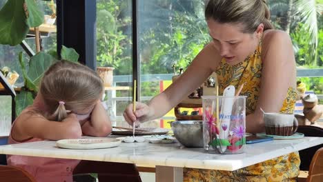 mother and daughter painting pottery in a cafe