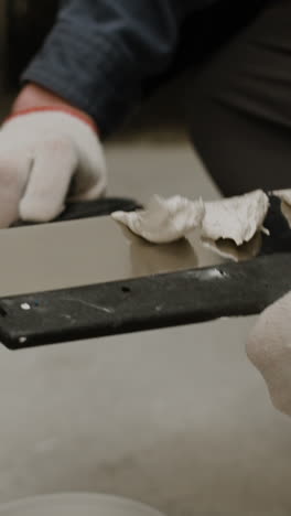 close-up of a person's hands using a putty knife to apply putty to a surface