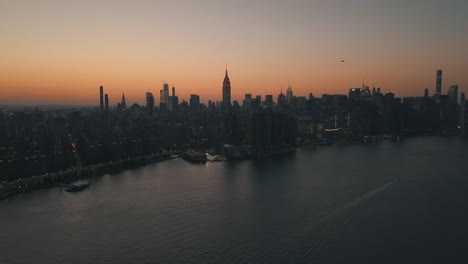 AERIAL:-Over-East-River-overlooking-Manhattan-New-York-City-Skyline-in-Beautiful-Dawn-Sunset-Orange-Light