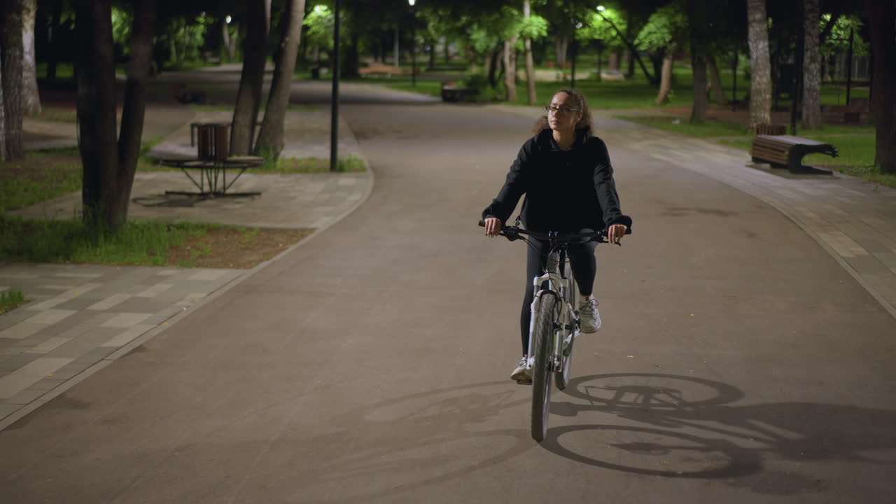 Adolescent Exploring Serene Outdoor Pathways Under Soft Lamplight, Young Student Steadily Cycling Through Tranquil Green Surroundings With Contemplative Mood And Gentle Illumination
