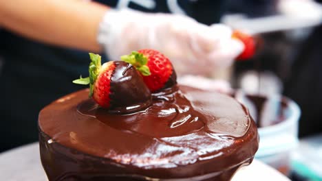 baker dipping strawberries in chocolate for cake decoration