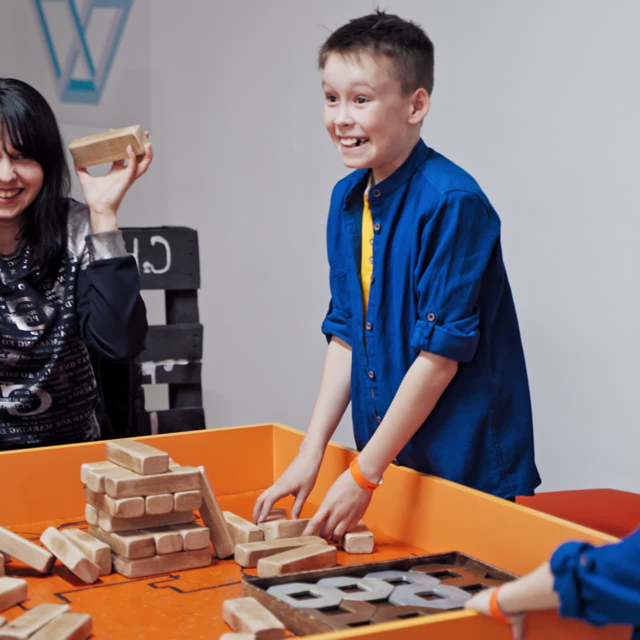 Happy boys and mother playing wooden tower table game together. Jenga falls on the table. The tower falls.