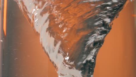 Static-slow-motion-shot-of-a-spinning-or-circling-water-vortex-or-water-tornado-in-front-of-orange-background