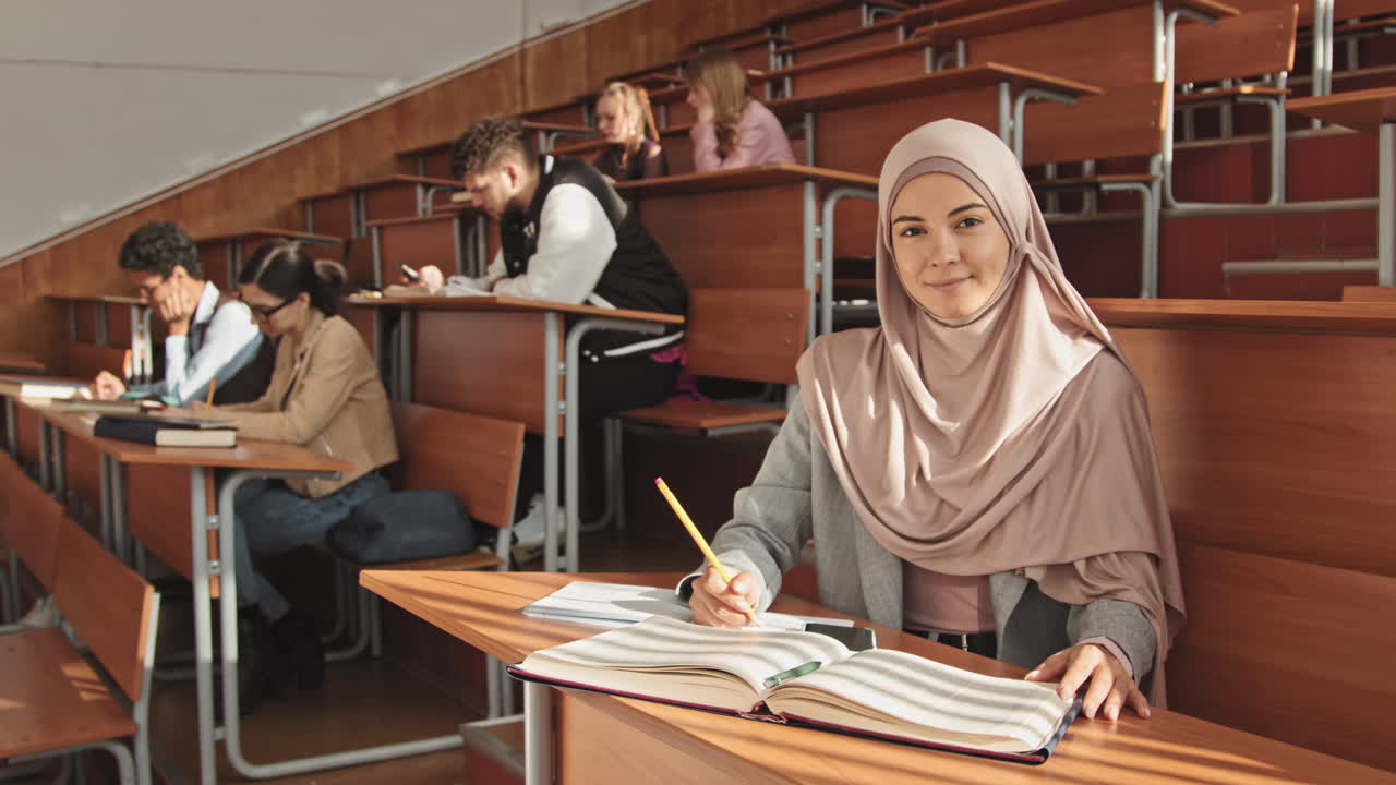 Portrait of Muslim Female Student Sitting by Desk in Auditorium