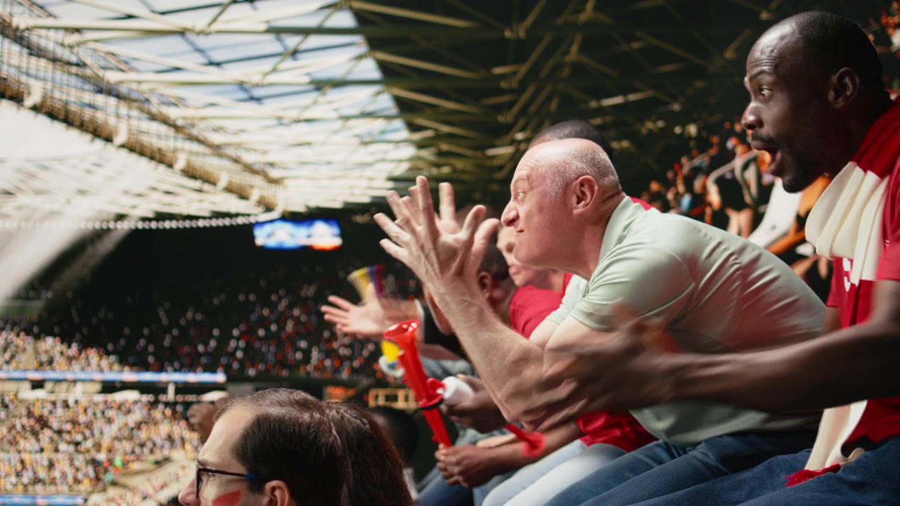 Frustrerede fodboldfans gestikulerer med åbne hænder på stadiontribunen.