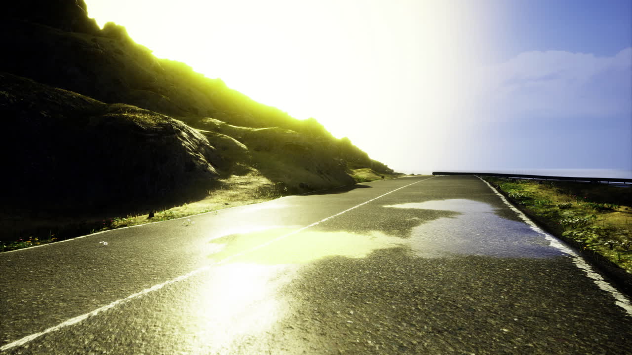 Bright sun reflecting on a wet road near a hillside in the afternoon