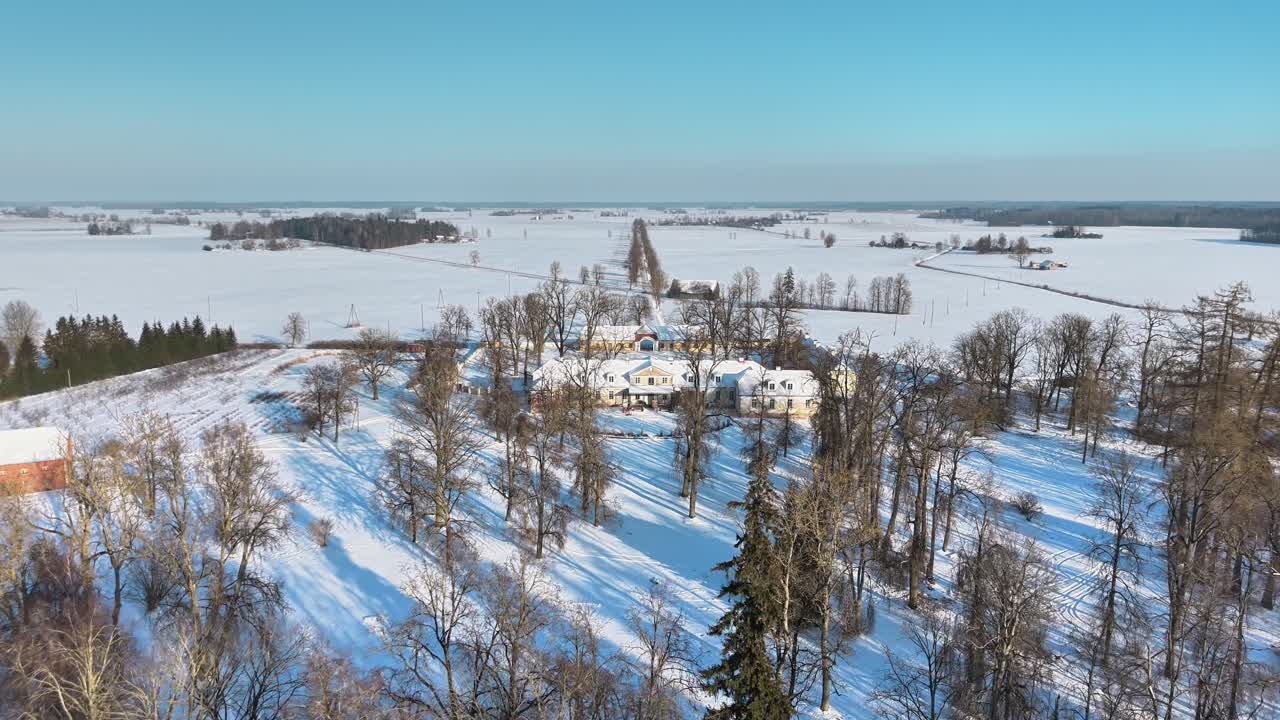 Snødekket landskap på landsbygda, flygende over tretoppene mot et stort landsted, Polen
