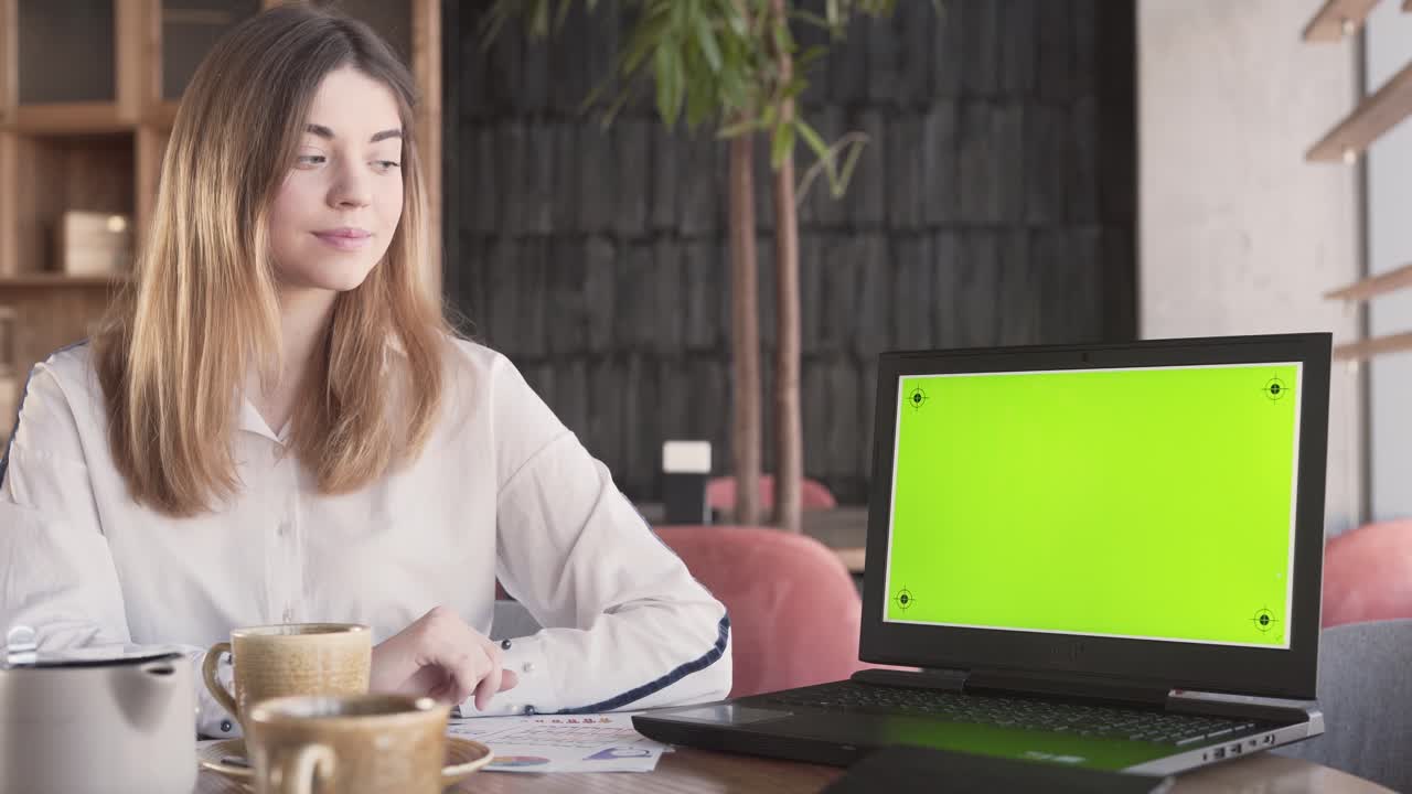 una joven encantadora está sentada cerca de la laptop mostrando una pantalla verde