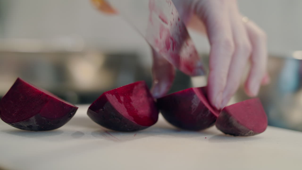 Una chef taglia con cura ed esperienza vivaci barbabietole a spicchi nella sua cucina pulita. Concetto di cucina vegetariana sana