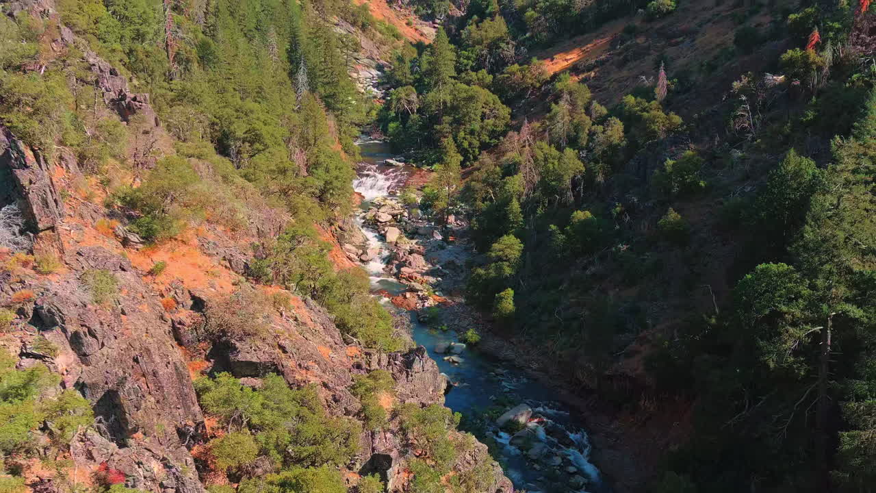 río que fluye a través de paisaje de montaña rocosa con bosque de pinos, revelación aérea retiro