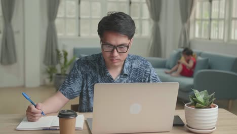 Man Working With Laptop Computer, His Son Sitting On Sofa And Watching On Mobile Phone, Video In 4K