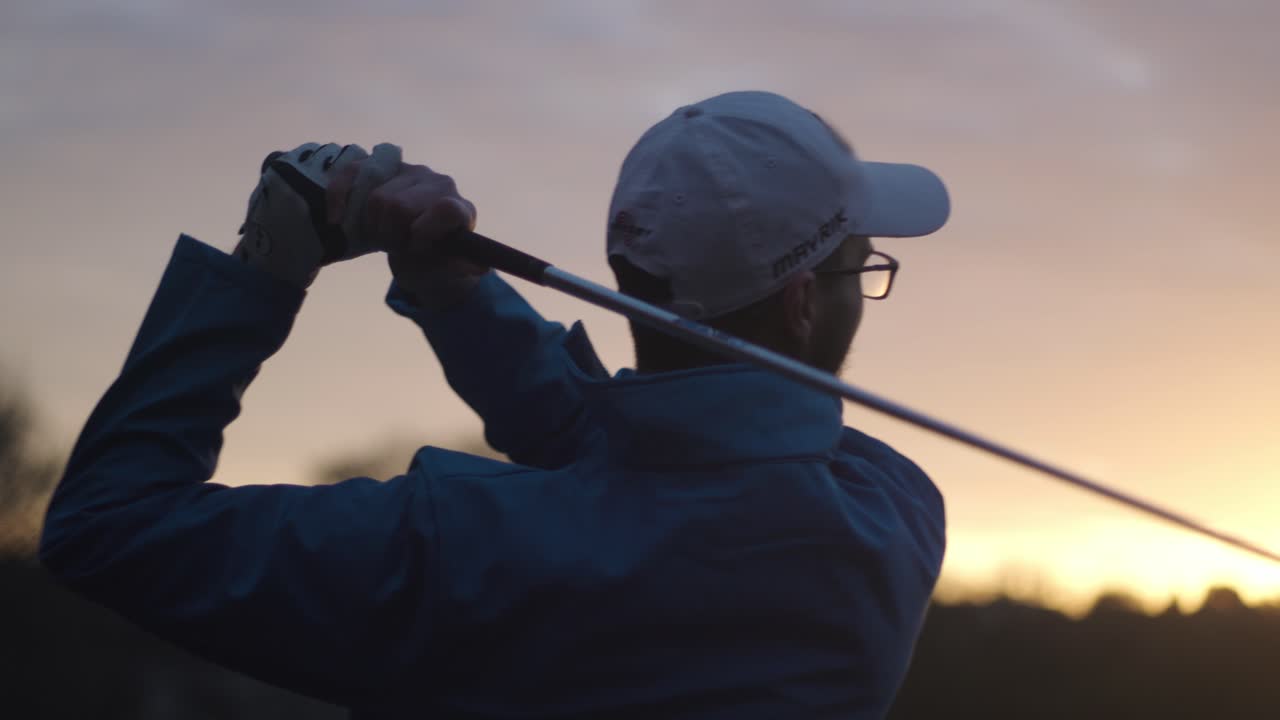 Close-up shot of a male golfer in cap and glasses taking a golf swing during golden hour at outdoor setting