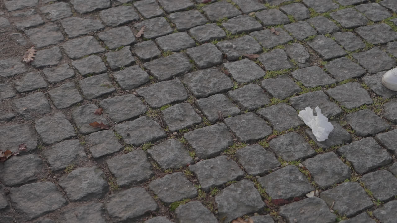 Person collecting trash from stone pavement at ground level