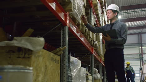 Hombre-De-Negocios-Con-Ropa-Elegante-En-El-Almacén-Clasificando-Cajas-Grandes-Mientras-Está-De-Pie-En-El-Pasillo-Junto-A-Un-Enorme-Estante-Con-Productos-Empaquetados