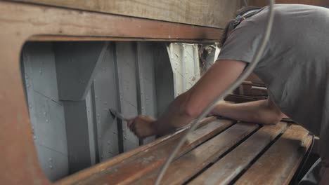 Young-man-wearing-mask-painting-interior-walls-of-wooden-boat