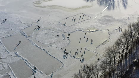 Vista-Aérea-De-Personas-Patinando-Sobre-Hielo-En-Un-Lago-Congelado,-Patinadores-Divirtiéndose-En-El-Soleado-Día-De-Invierno