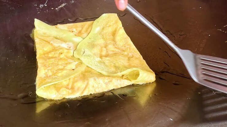 A detailed view of a roti being flipped and cooked on a hot griddle using a spatula.