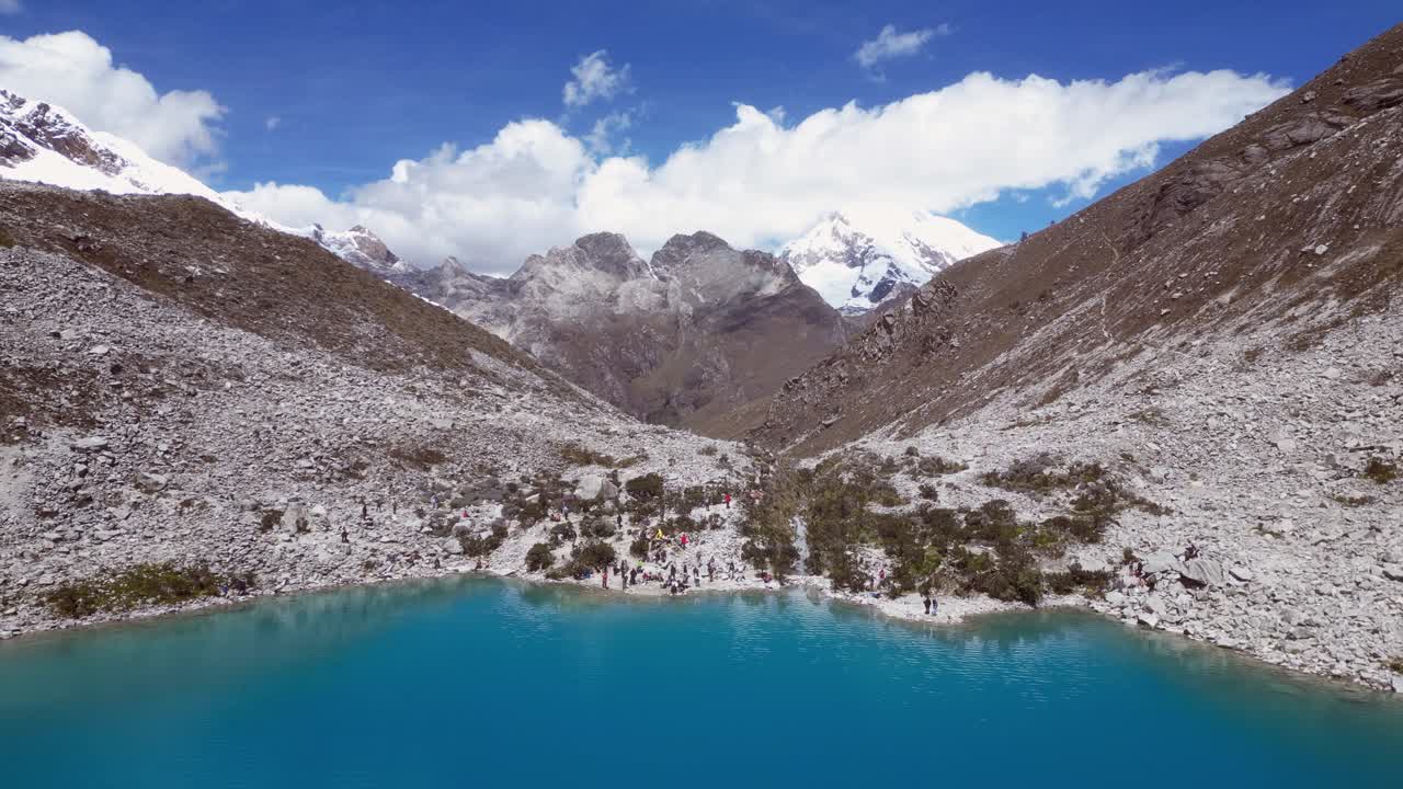 Tourists gather on shoreline of small alpine mountain tarn in Peru