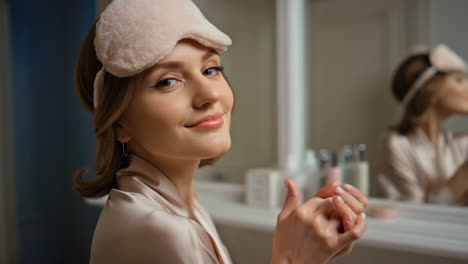 young woman in silk robe and eye mask applying hand cream as part of her skincare routine