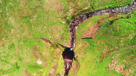 high aerial top down shot of a winding stream in the middle of the countryside, bright summers day