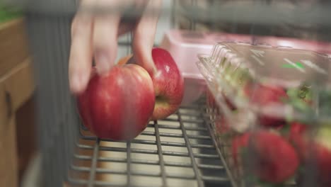 apples getting kept by an unknow person in cart in a grocery store.
