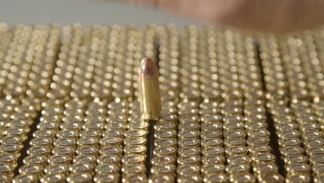 Hand-grabbing-9-millimeter-bullets-stacked-on-brand-new-ammunition,-leaving-a-single-round