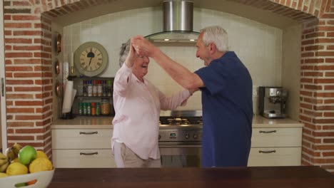 Senior-caucasian-couple-dancing-in-kitchen-in-slow-motion