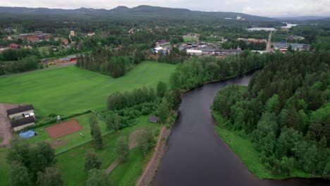 person running along river, small town and green landscape, backward aerial