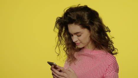 Young-woman-using-mobile-phone-on-yellow.-Woman-typing-message-on-mobile-phone